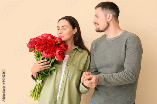 Happy engaged couple with flowers holding hands on beige background