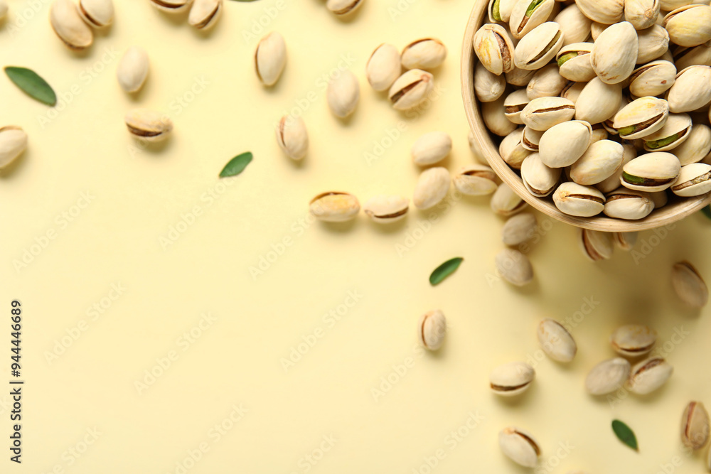 Bowl with tasty pistachio nuts and leaves on yellow background Bowl with tasty pistachio nuts and leaves on yellow background