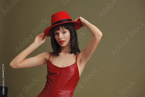 Woman in red dress and hat, posing with hands on head, hair pulled back, background neutral, elegant and confident demeanor, high fashion concept