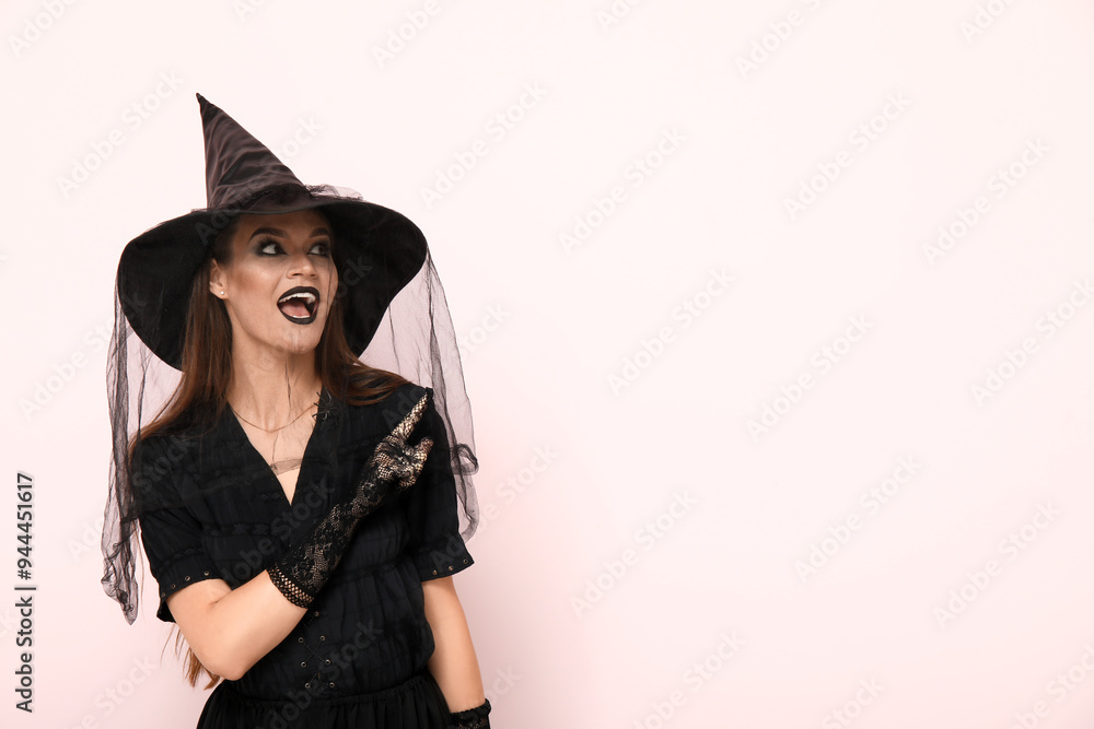 Young woman dressed for Halloween as witch pointing at something on light background Young woman dressed for Halloween as witch pointing at something on light background