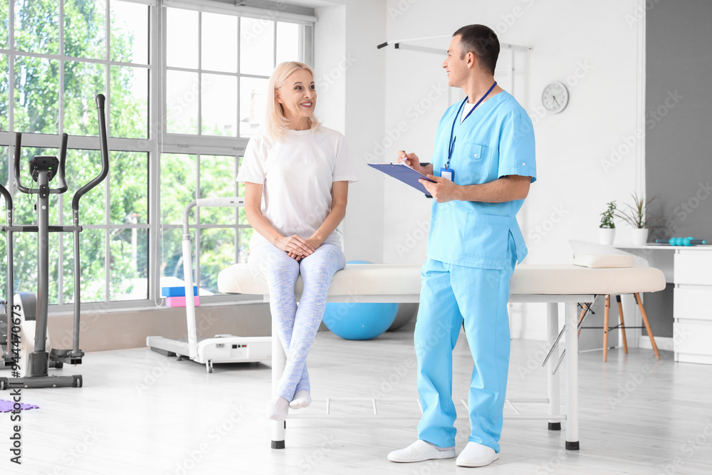 Fototapeta premium Male physiotherapist with clipboard and mature woman in rehabilitation center