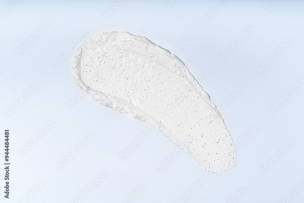 Fototapeta premium A white smear of face scrub on a light blue background, isolated smudge