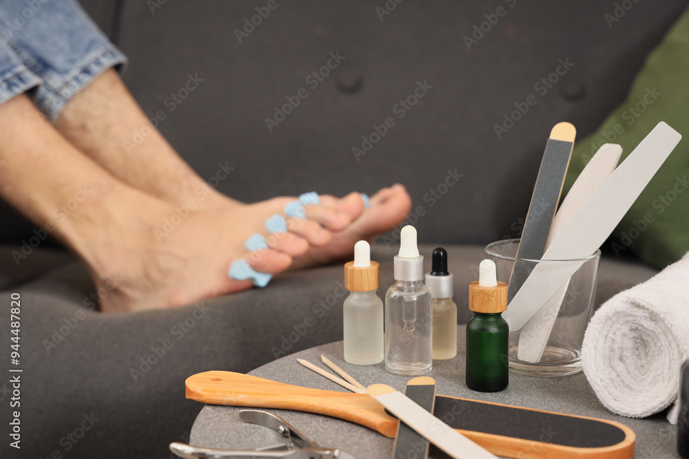 Fototapeta premium Feet of young man with tools, toe separator and fresh pedicure at home, closeup