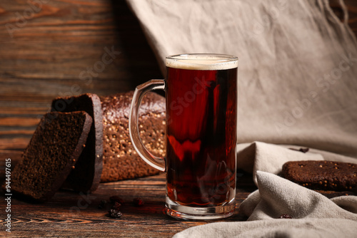 Mug of fresh kvass and bread on wooden background photo