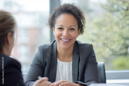 a smiling mid age mixed race female businesswoman, banker, financial director sitting in the office at the table, looking at the camera.  photo