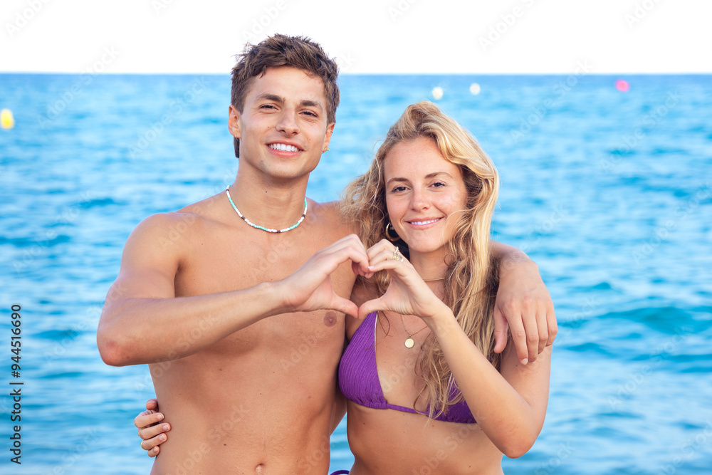 Young couple making heart shape with their hands on the beach looking at camera Young couple making heart shape with their hands on the beach looking at camera
