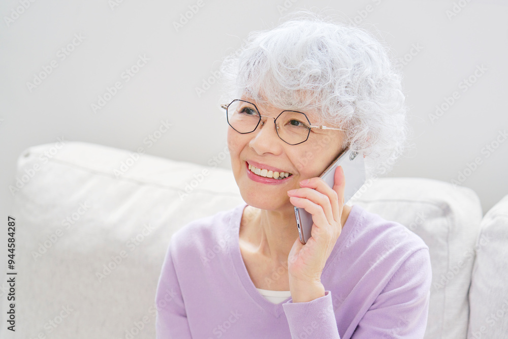 スマートフォンで電話するシニア女性 リビングルーム スマートフォンで電話するシニア女性 リビングルーム
