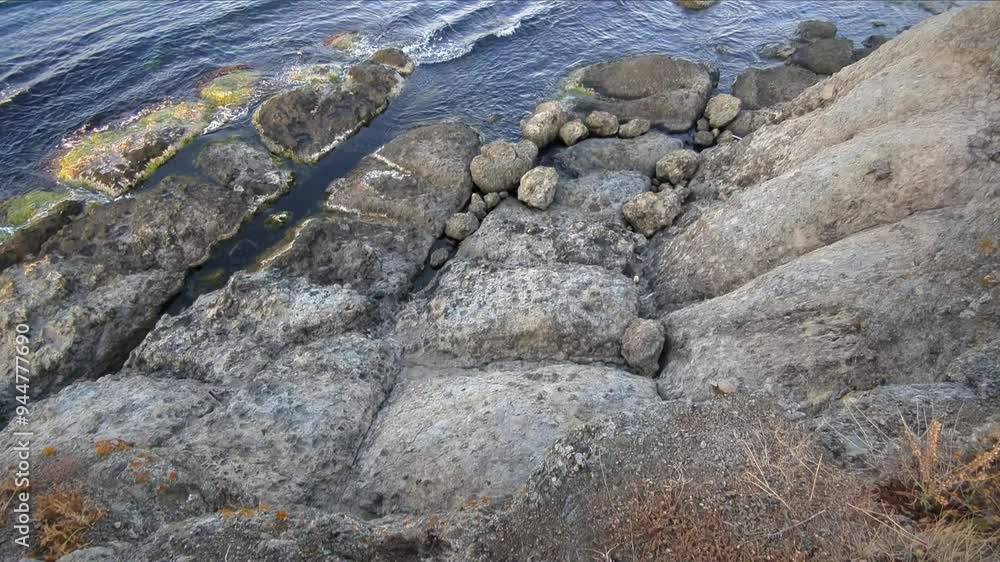 A panoramic view of towering rocky cliffs and the sea with waves crashing against the shore. A panoramic view of towering rocky cliffs and the sea with waves crashing against the shore.