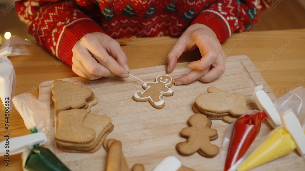 Hands in a Red Sweater Decorate Gingerbread Cookies on a Wooden Board Using Icing, With Various Cookie Shapes and Icing Bags in the Background. Hands in a Red Sweater Decorate Gingerbread Cookies on a Wooden Board Using Icing, With Various Cookie Shapes and Icing Bags in the Background.