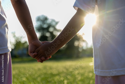 Two children holding hands in a grassy field.