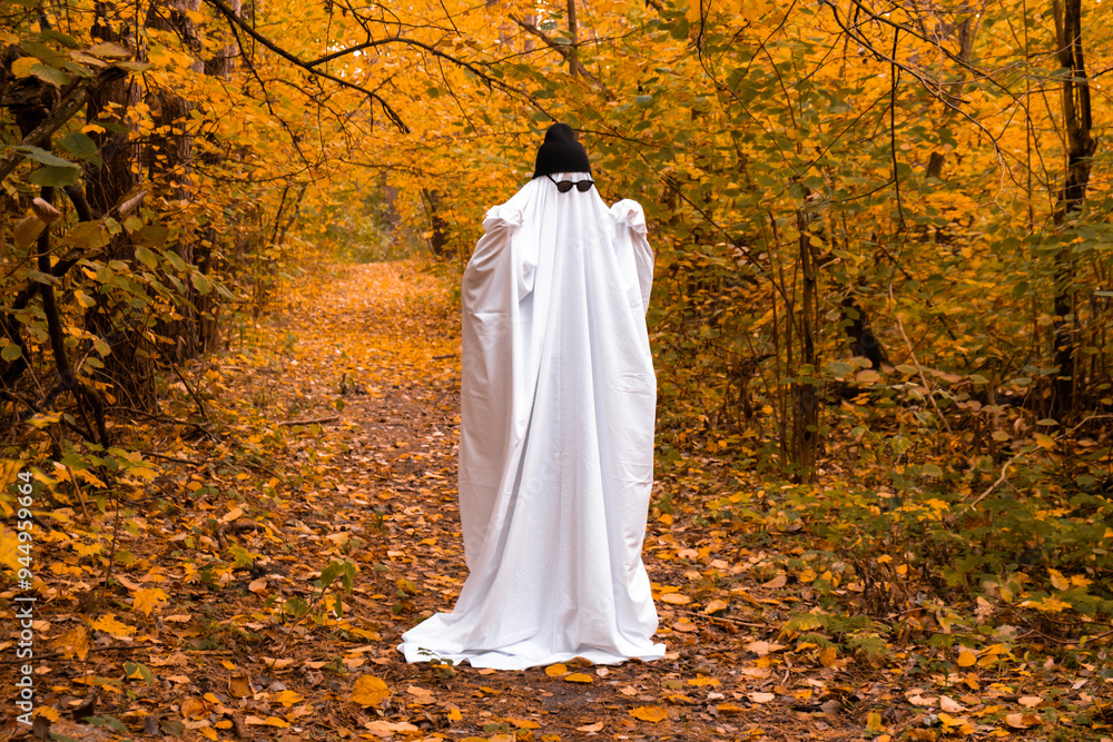 Happy Halloween holiday. Cute unrecognizable person in ghost costume on fall forest background. Creative costume with white and black cap hat and glasses. Minimal concept
