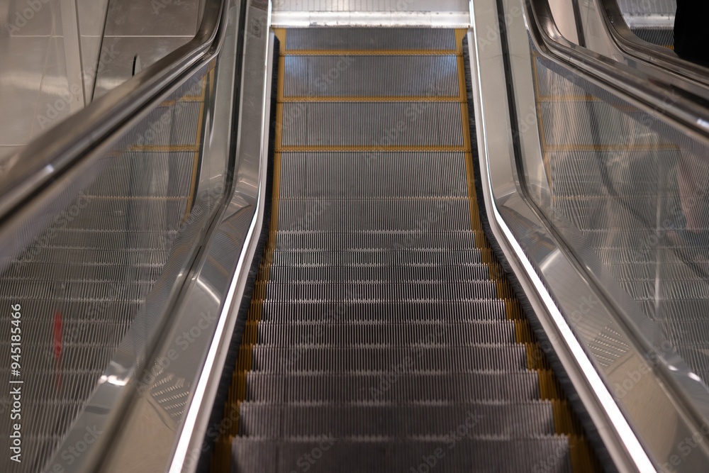 Empty escalator in a subway station, with metal steps and illuminated handrails unoccupied and awaiting passengers Empty escalator in a subway station, with metal steps and illuminated handrails unoccupied and awaiting passengers