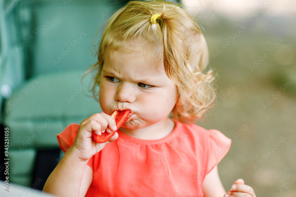 Little toddler girl eating red pepper and vegetables for healthy lunch snack sitting in baby stroller. happy child and healthy food Little toddler girl eating red pepper and vegetables for healthy lunch snack sitting in baby stroller. happy child and healthy food