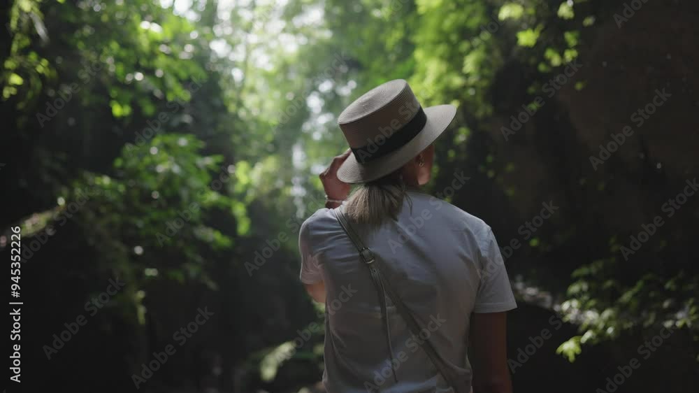 Young adult woman in beautiful rainforest in sunny summer day, back view. Slender lady enjoying beauty of tropical woodland and nature, water falling from up, slow motion, fairytale trip to jungle Young adult woman in beautiful rainforest in sunny summer day, back view. Slender lady enjoying beauty of tropical woodland and nature, water falling from up, slow motion, fairytale trip to jungle