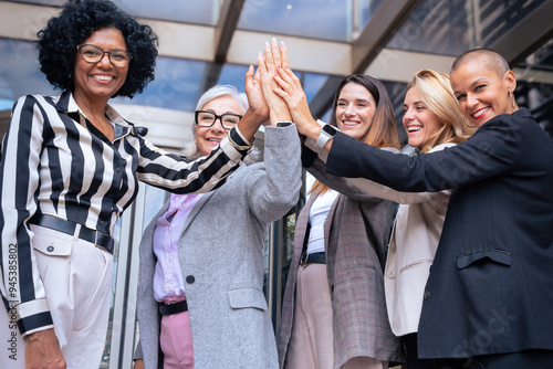 Group of five smiling businesswomen shaking hands outdoors.