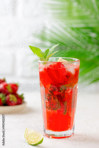 Cold mojito cocktail with strawberries, lime and mint on a background of a palm branch. Strawberry Mojito. Sugar free, nonalcoholic. Vertical orientation.