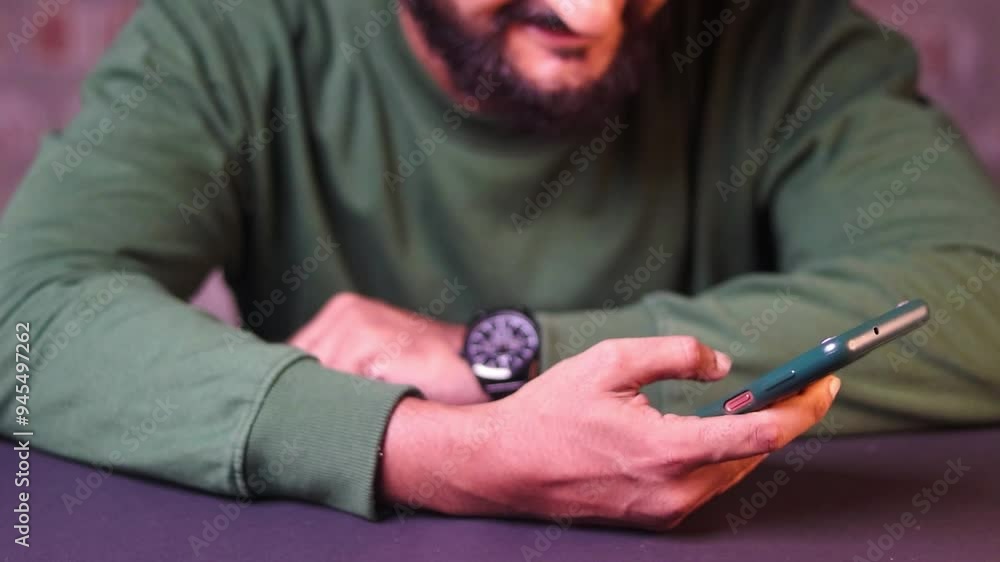 Close-up shot of man's hands, a businessman in green pullover and beard wearing black watch and holding phone, typing message, scrolling, close-up and smiling Close-up shot of man's hands, a businessman in green pullover and beard wearing black watch and holding phone, typing message, scrolling, close-up and smiling