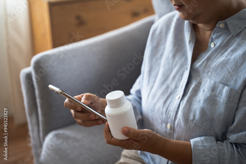 Health care Asian senior woman using smart phone to reading, searching prescription on bottle medicine, pill label text about information online, instructions side effects, pharmacy medicament