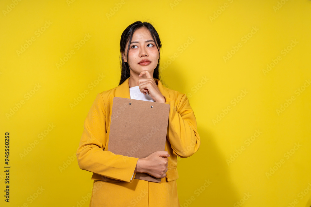 Obraz premium A woman in a yellow jacket is holding a clipboard and looking to her right