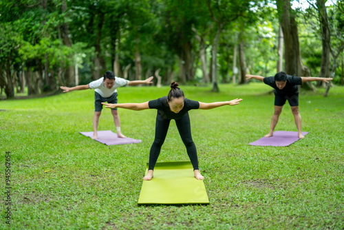 Three people are doing yoga on a green mat in a park