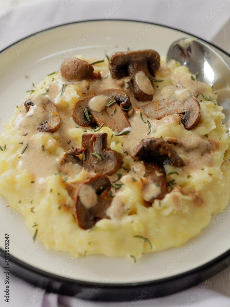 A plate of creamy mashed potatoes topped with a rich mushroom gravy and garnished with fresh rosemary. The dish is elegantly presented on a white plate, highlighting the hearty, comforting meal. A plate of creamy mashed potatoes topped with a rich mushroom gravy and garnished with fresh rosemary. The dish is elegantly presented on a white plate, highlighting the hearty, comforting meal.