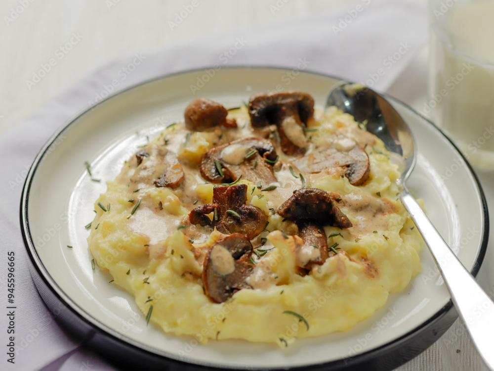 A plate of creamy mashed potatoes topped with a rich mushroom gravy and garnished with fresh rosemary. The dish is elegantly presented on a white plate, highlighting the hearty, comforting meal. A plate of creamy mashed potatoes topped with a rich mushroom gravy and garnished with fresh rosemary. The dish is elegantly presented on a white plate, highlighting the hearty, comforting meal.