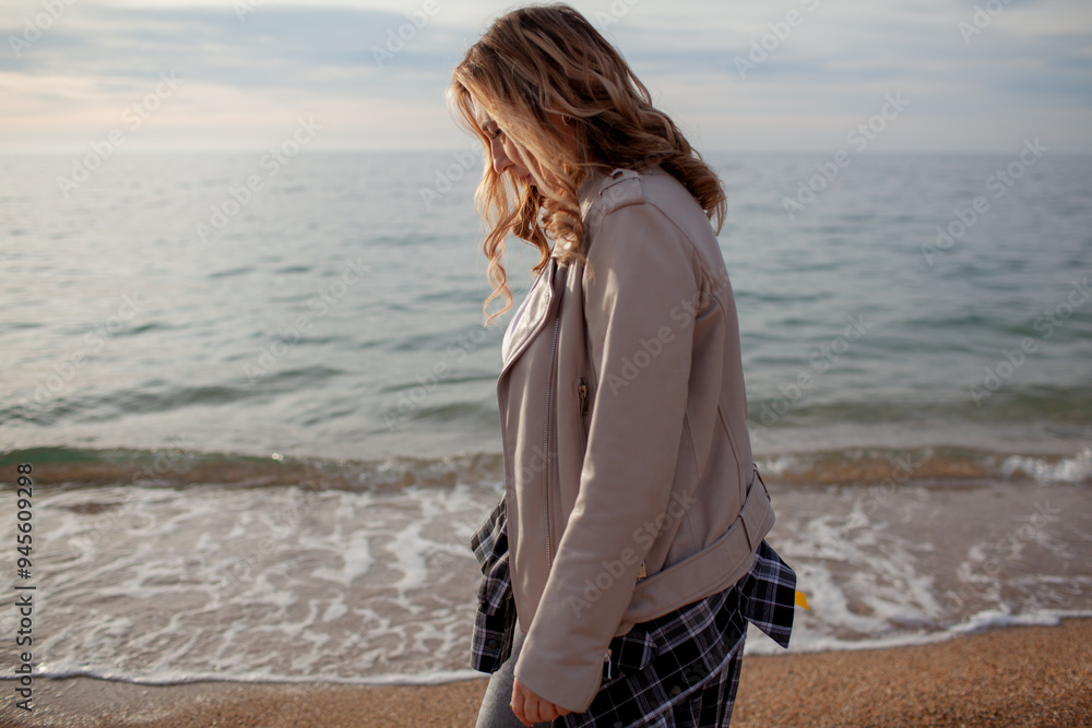 A beautiful middle-aged woman walks on a sandy beach in autumn or spring. A 45-year-old woman is wearing jeans, a beige jacket and a plaid shirt. The model enjoys relaxation and a quiet environment A beautiful middle-aged woman walks on a sandy beach in autumn or spring. A 45-year-old woman is wearing jeans, a beige jacket and a plaid shirt. The model enjoys relaxation and a quiet environment