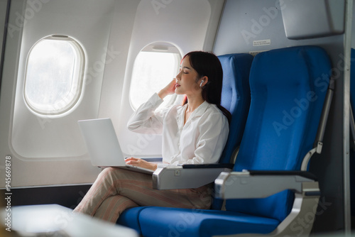 Bilde på lerret Businesswoman on a Flight: A professional woman in a white shirt and slacks, working on her laptop while seated in an airplane, showcasing the modern business traveler's lifestyle