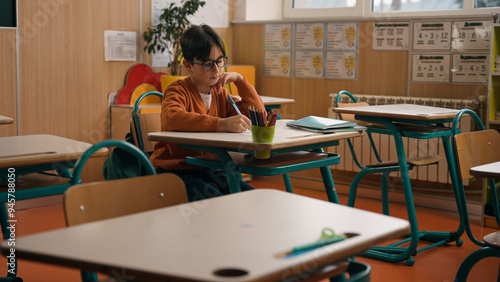 Fotografie Alone little boy in empty school class room sitting at desk table writing homewo