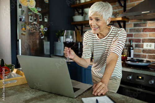 Senior woman enjoying virtual wine chat on laptop at home photo