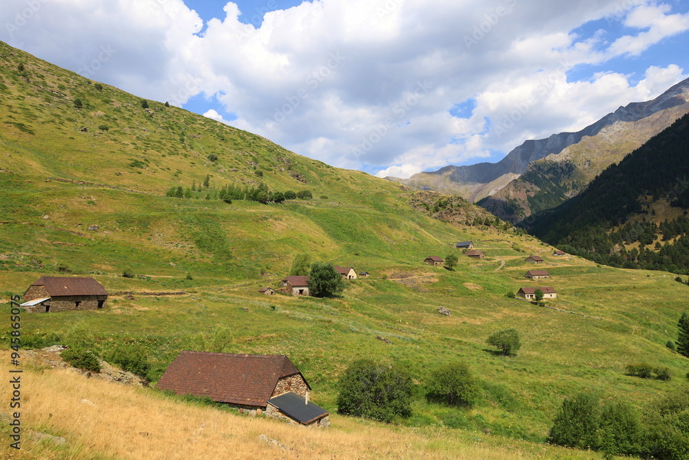 Historiacal Viados village in Spanish Pyrenees. Old, stone shepherd's huts among green meadows, with huge, rocky walls of Posets Massif fulfilling upper parts of the image next to Benasque Historiacal Viados village in Spanish Pyrenees. Old, stone shepherd's huts among green meadows, with huge, rocky walls of Posets Massif fulfilling upper parts of the image next to Benasque