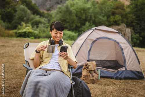 Mature japanese woman sit in front of tent and use mobile phone