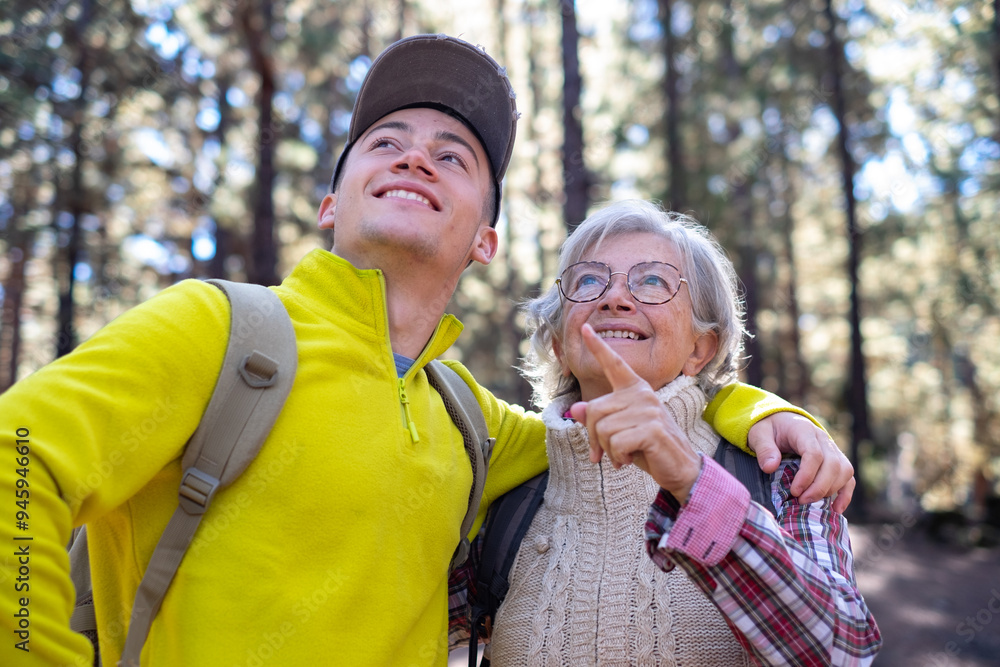 © luciano - Couple of happy grandmother and young grandson in trekking day in the forest looking the nature, young and old people enjoying together outdoors excursion