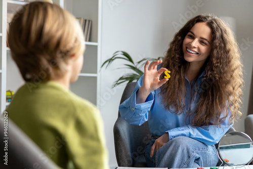 Long-haired young speech therapist working with a blonde boy and both looking involved