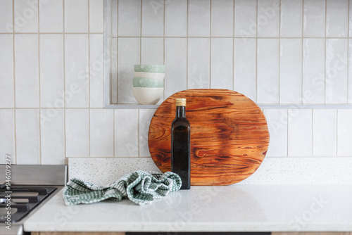 Styled surface on a modern white stone kitchen counter with white vertical wall tiles. Wooden cutting board, green kitchen towel cloth, small bowls and bottle of olive oil