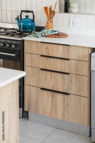 Wood look kitchen cabinet drawers with a white stone counter top, hidden black handles, black free standing cooker and styled kitchen elements