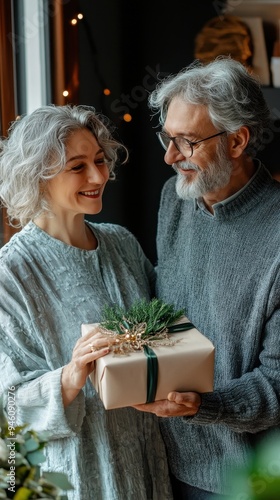 An elderly couple smiles warmly at each other while holding a wrapped gift, capturing the joy of sharing moments together at home