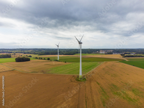 Aerial side view of two windmills in the wind. Sweden, summer, green and yellow fields and farmland. Cloudy with sunrays piercing through