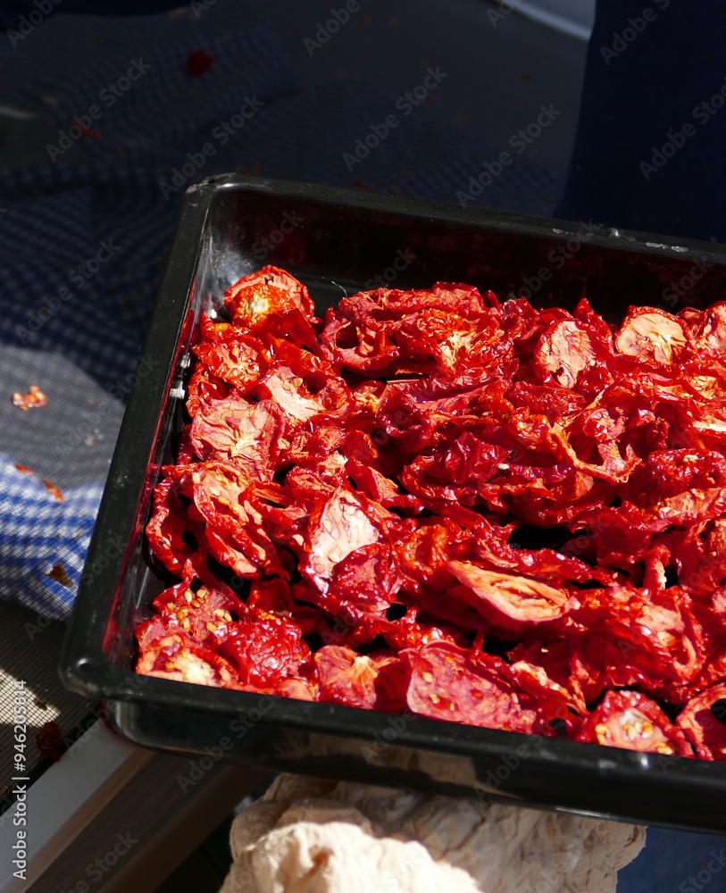 A woman collects dried tomatoes into a container.