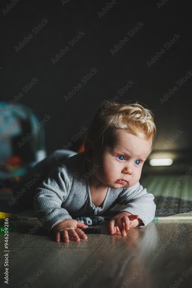 Fototapeta premium Cute blond toddler boy playing with baby toys at home sitting on carpet in living room. Smiling cute little child using colorful toys, chewing teether
