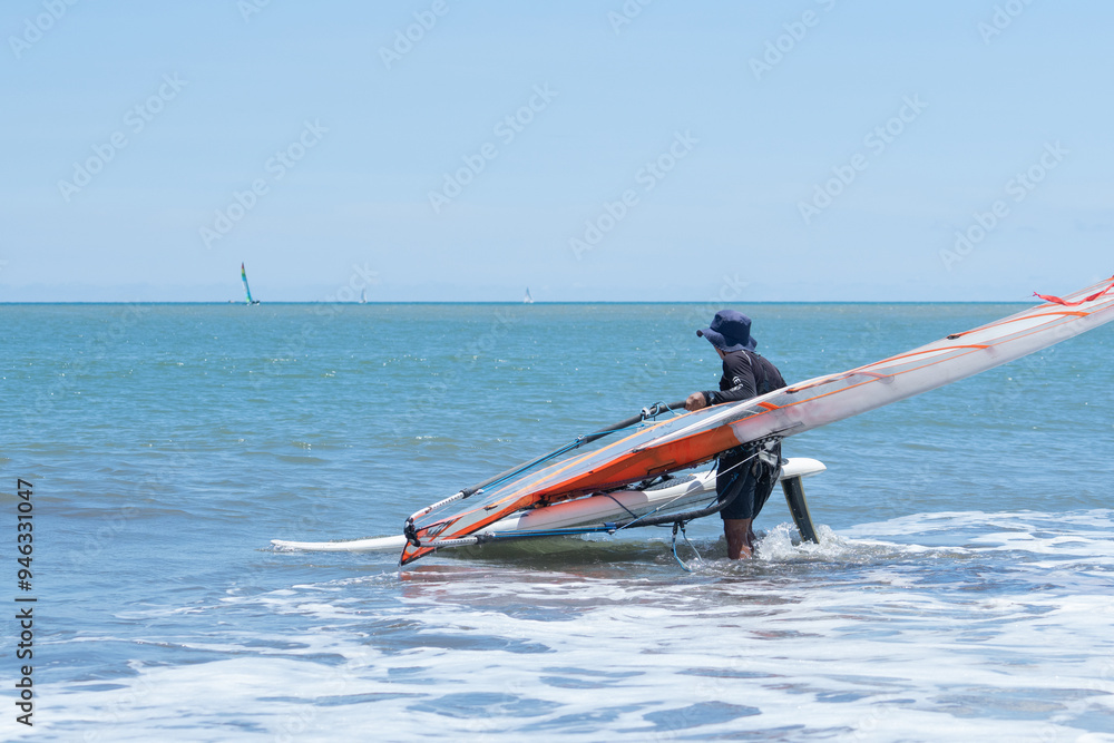 Naklejka premium A male surfer prepares for windsurfing on the beach