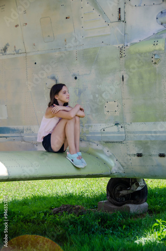 Preteen girl sitting near small helicopter at airfield photo