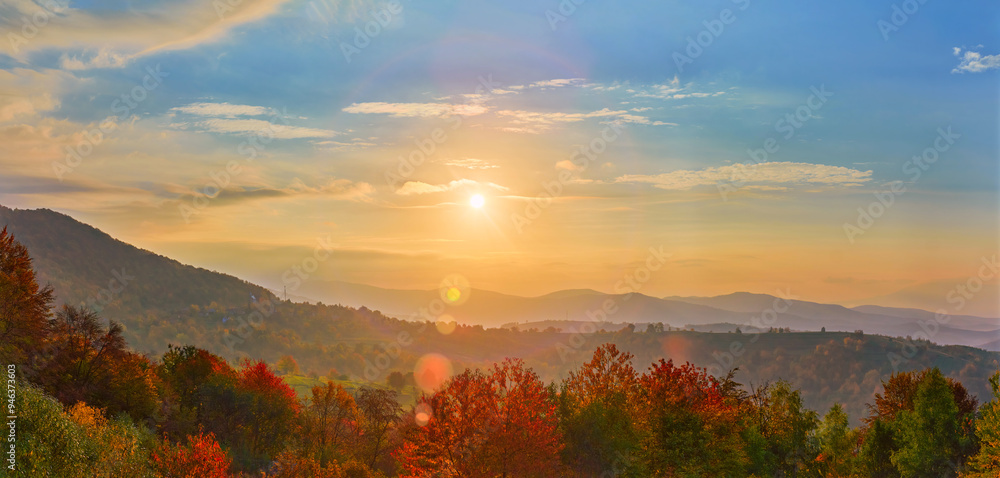 Fototapeta premium A breathtaking sunrise over a mountainous landscape. The golden light bathes the misty hills and colorful autumn trees, creating a warm, peaceful ambiance under a sky brushed with clouds