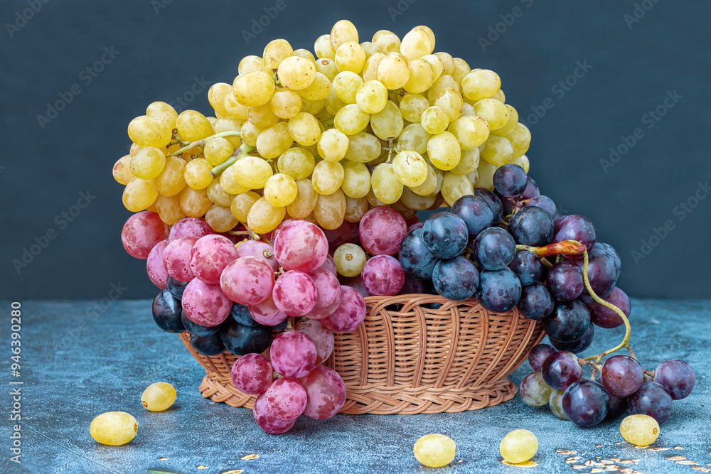 Yellow, black and red grapes in a wicker basket on a table.