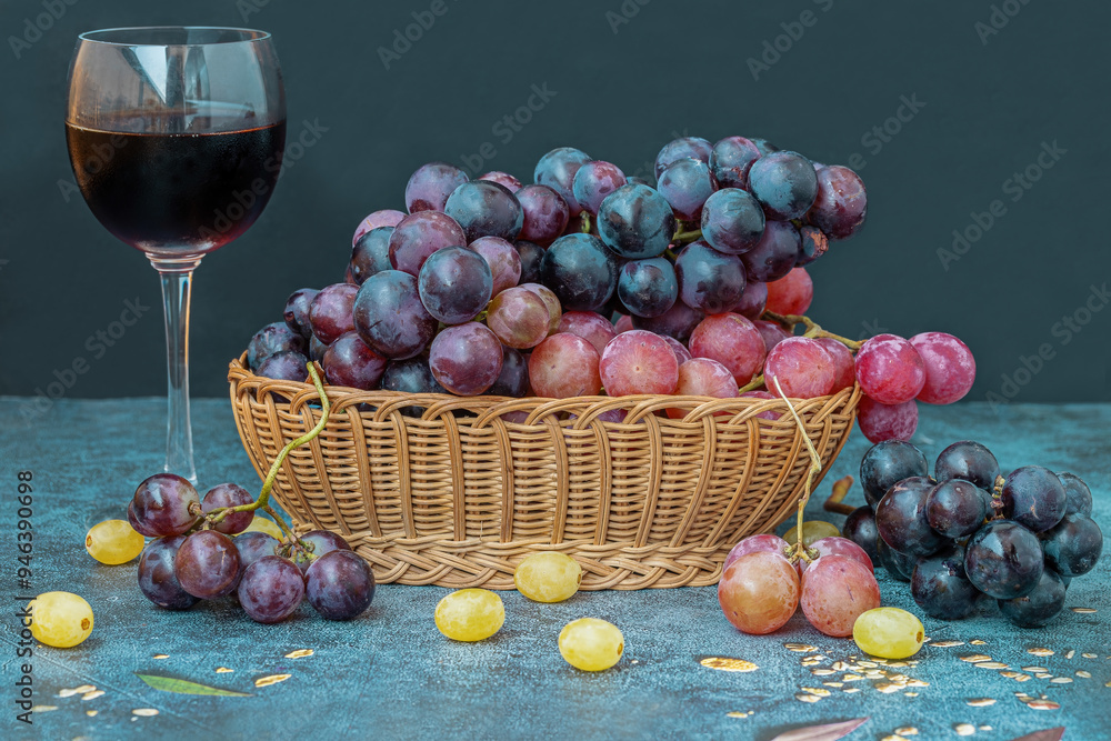 Black grapes on a table, red grapes in a basket and a glass of red wine on the table