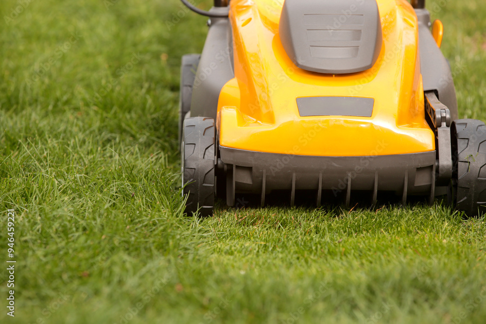 Fototapeta premium Yellow lawn mower on the spring green grass in the yard