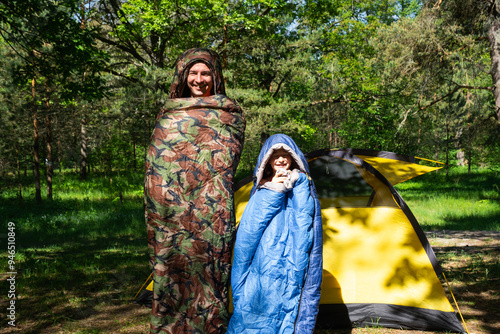 Family of tourists from a father and daughter pose and Funny dancing in sleeping bags near a tent. Family outdoor recreation, camping, hiking equipment.  photo