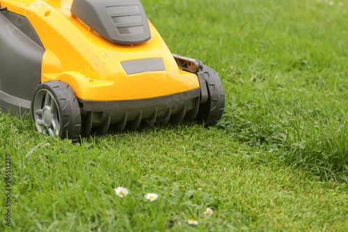 Yellow lawn mower on the spring green grass in the yard