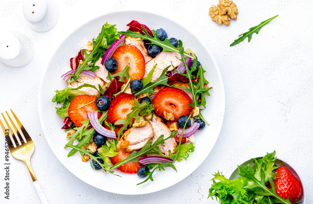 Strawberry and chicken fresh salad with arugula, blueberries, onion and walnuts, white background, top view Strawberry and chicken fresh salad with arugula, blueberries, onion and walnuts, white background, top view