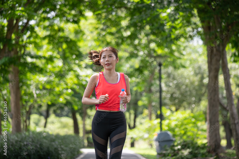Asian female runner running on the street and holding water bottle in the park Asian female runner running on the street and holding water bottle in the park